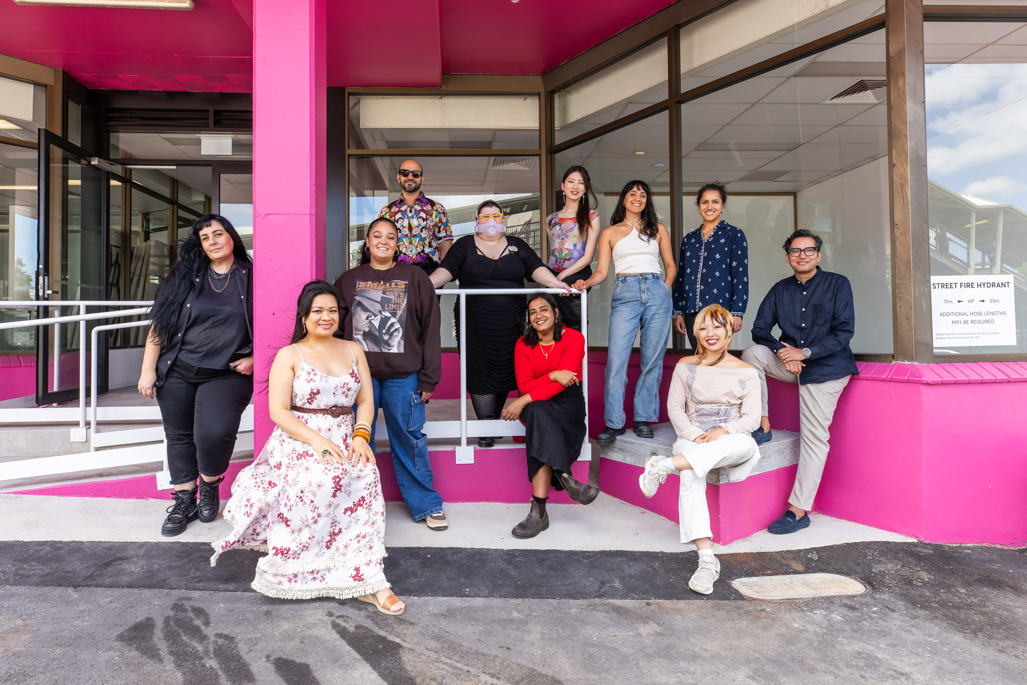 A group of people gathered together in front of a pink building facing the camera