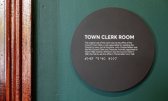 Close up image of a circular black sign on the wall for the Town Clerk Room, with a detailed explanation below