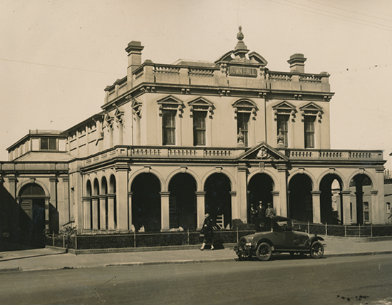 Historical black and white image of the town hall, with a car and people in front of it