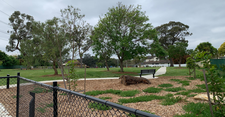 Fence on left, park with bench and trees