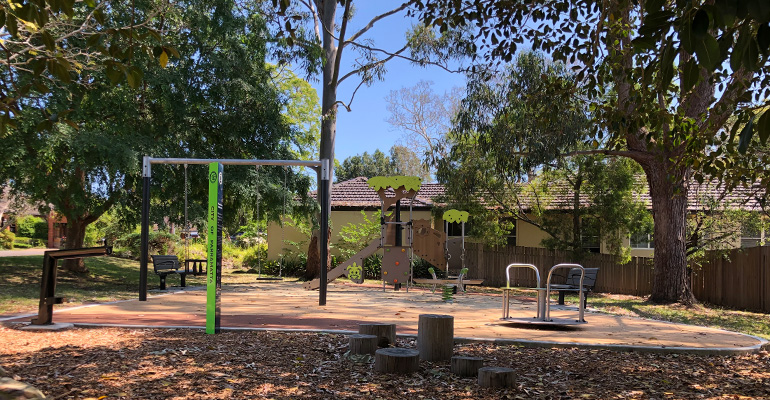 Playground with swings, slides, merry-go-round and park bench shaded by trees
