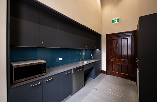 Image of a basic modern kitchen with dark blue cabinets, a teal splashboard, microwave and sink