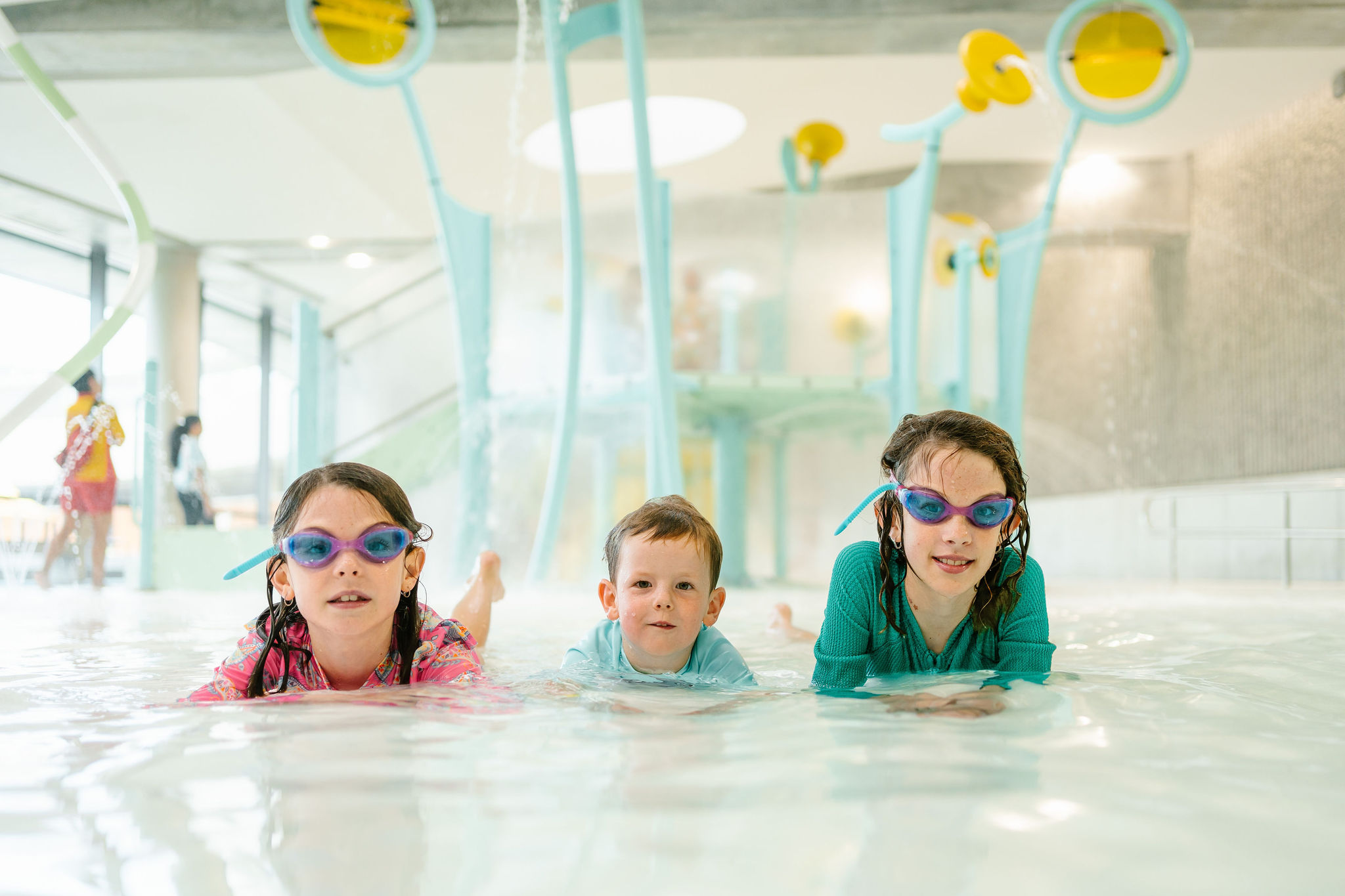 Two girls and a boy laying in the splash play area