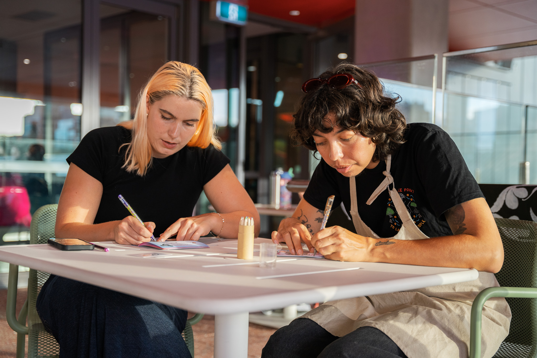 Two women sitting at table writing on paper