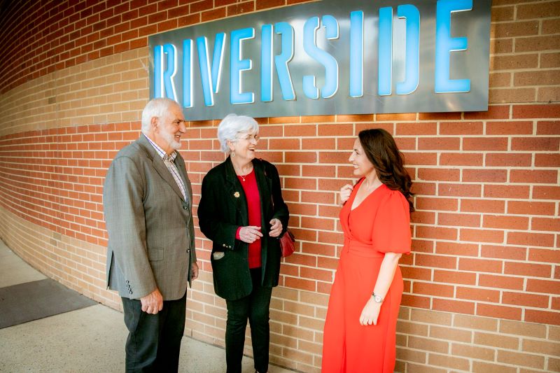 Two Women and Man in front of Riverside sign and building smiling