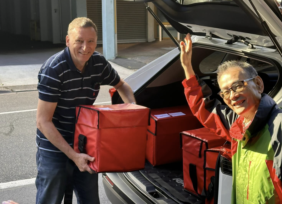 Two men taking meal bags from car