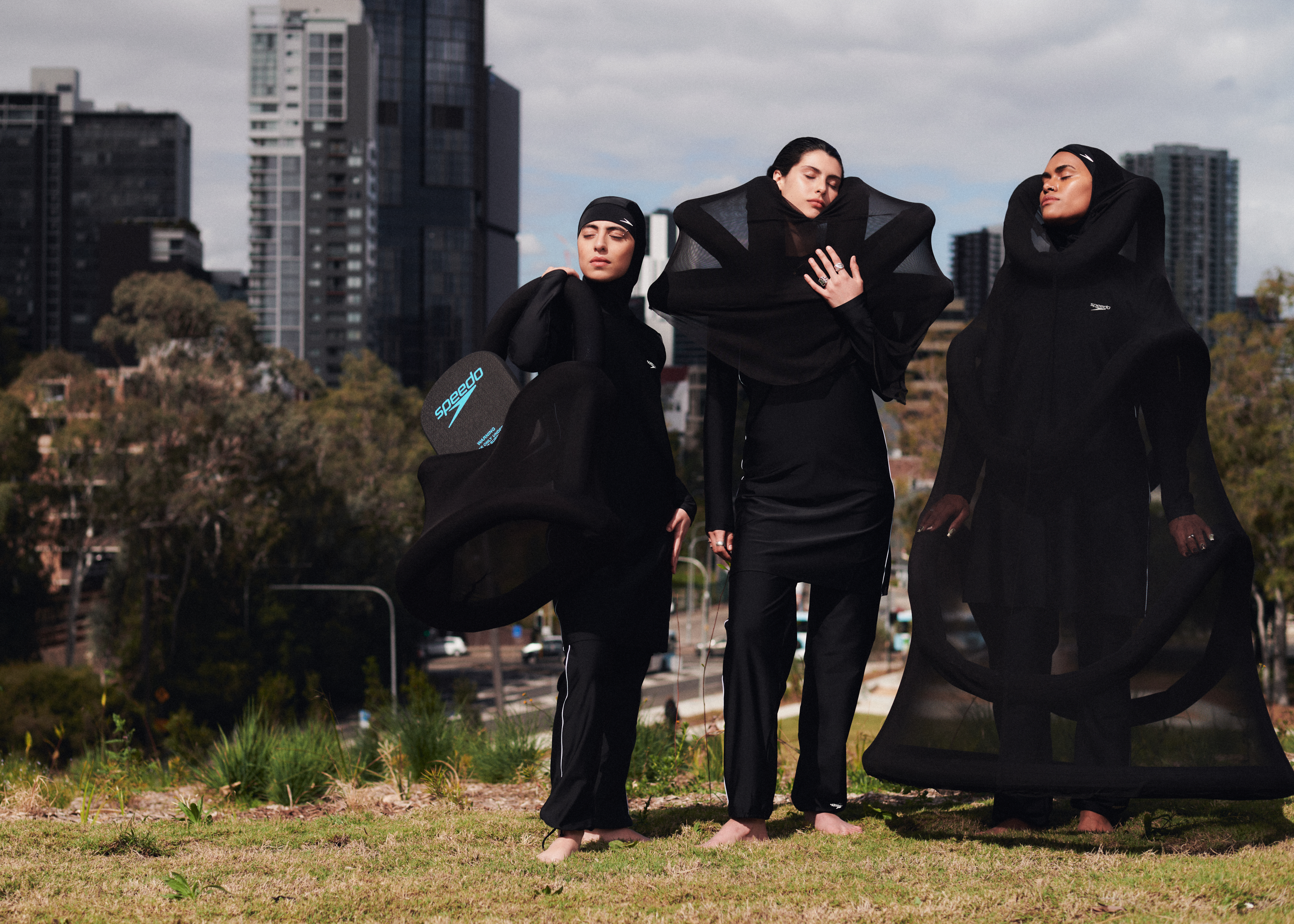 A group of hijabi models in black clothing on top of a hill framed by a city skyline