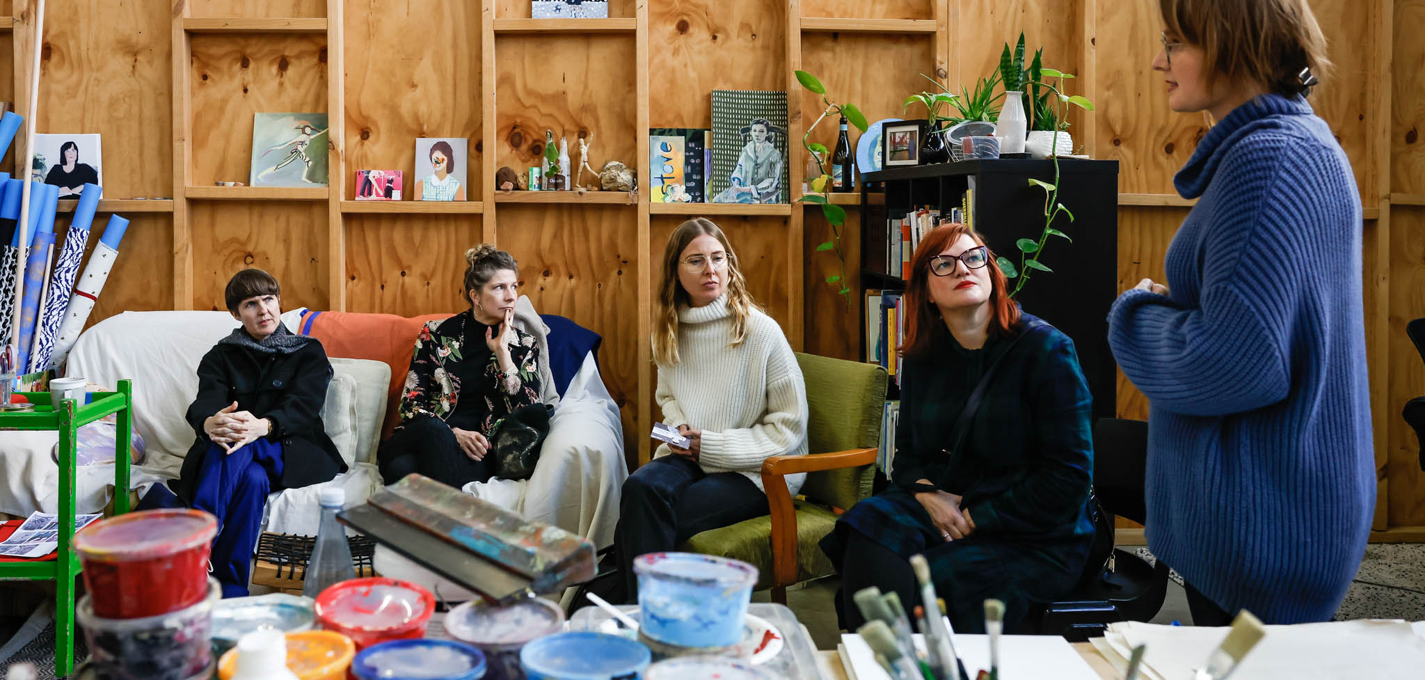A group of women gathered and talking inside a studio filled with art and materials