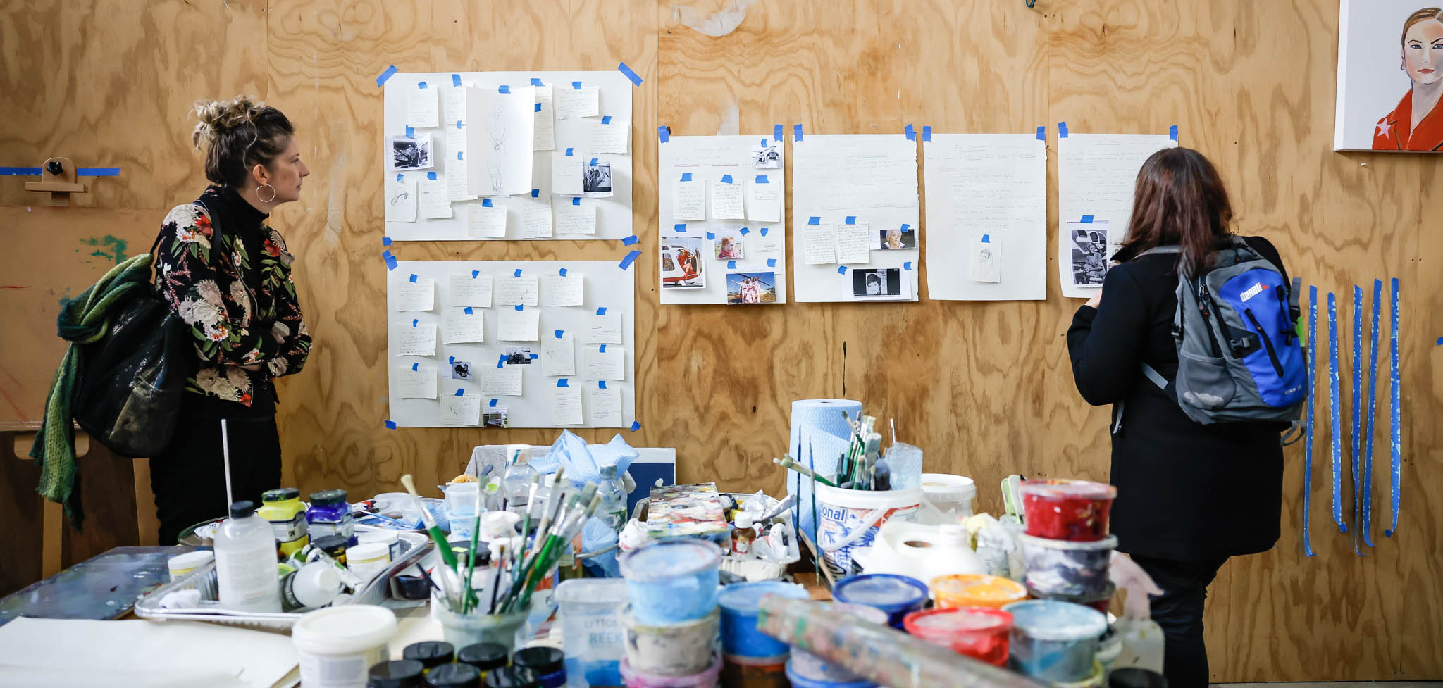 Two people inside an artist studio densely packed with painting materials