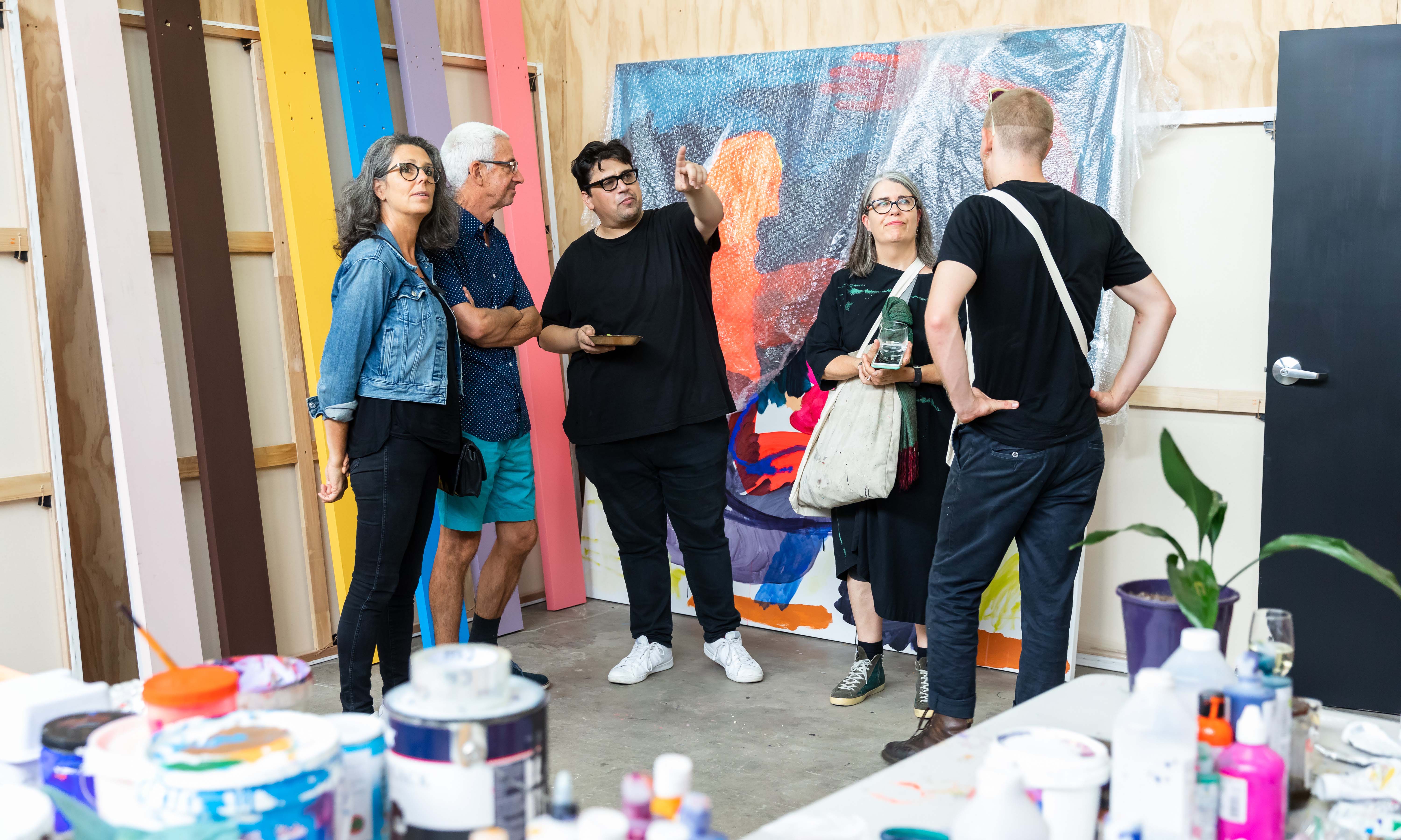 A group of people in a studio filled with bright paintings