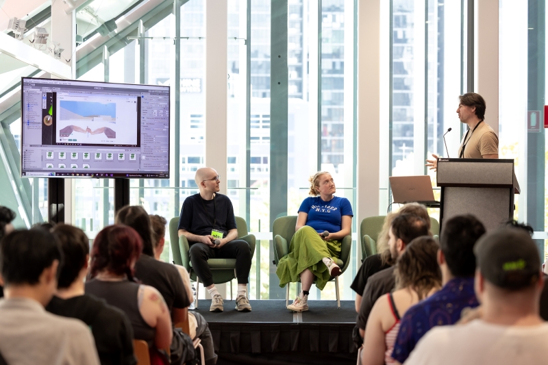 A conference panel features a speaker at a podium addressing two seated panelists. An audience listens intently. A screen displays a digital presentation.